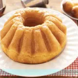 Un soffice babà a ciambella, lucido di bagna, pronto per essere gustato. Accanto, altri babà e una bottiglia di rum.