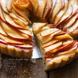 Una fetta di crostata di mele dorata, con mele caramellate disposte a rosa su una base friabile.