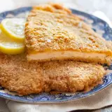 Due cotolette al forno dorate e croccanti, servite su un piatto blu con spicchi di limone.