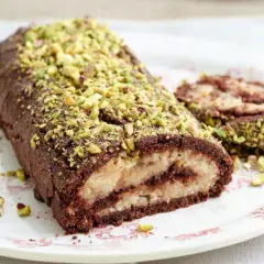 Rotolo al cioccolato e pistacchio, un dolce con farina di riso, ripieno di crema chiara e decorato con granella verde.