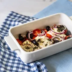 Feta al forno con pomodorini, olive nere e cipolla rossa, condita con erbe aromatiche.