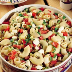 Un invitante piatto di pasta fredda con zucchine, pomodorini, cubetti di formaggio e fagioli, perfetto per un pasto estivo.