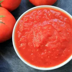 Una ciotola di passata di pomodoro, con pomodori freschi sullo sfondo.