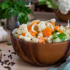 Una ciotola di legno piena di giardiniera fatta in casa, con cavolfiore, carote e cipolle, guarnita con prezzemolo fresco.