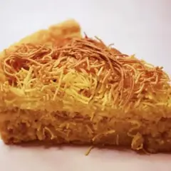 Una fetta di torta di tagliatelle, con la crosta dorata e un ripieno soffice, decorata con fili croccanti.