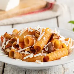 Piatto di pasta alla norma ricetta con melanzane fritte, pomodoro e ricotta salata grattugiata.