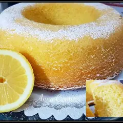 Un soffice ciambellone al limone, spolverato di zucchero a velo, accanto a una fetta di limone fresca.