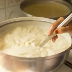 Mano che mescola un pentolone pieno di cremoso yogurt fatto in casa, pronto per essere gustato.