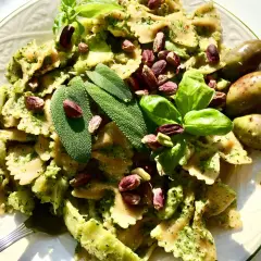 Farfalle condite con un cremoso pesto di salvia, guarnite con pistacchi, basilico e olive verdi.