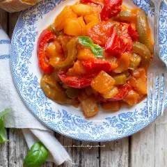 Un piatto di peperonata con patate, colorata e saporita, guarnita con basilico fresco.