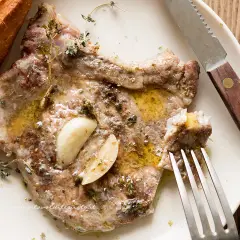 Succulente braciole di maiale cotte con aglio e erbe aromatiche, servite con pane croccante e un filo d'olio.