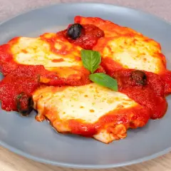 Delizioso pollo alla pizzaiola su un piatto grigio, con pomodoro, mozzarella filante, olive nere e una foglia di basilico.