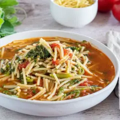 Un piatto fumante di pasta con i tenerumi, un classico siciliano, con pomodoro e verdure fresche.