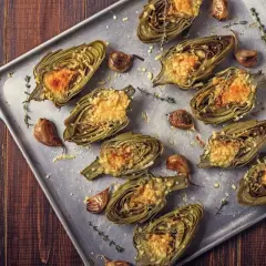 Carciofi al forno morbidi, ripieni e gratinati, con aglio e timo su teglia metallica.
