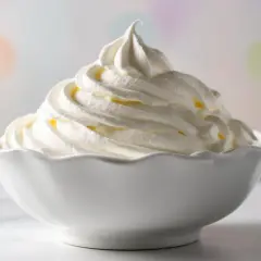 Una ciotola bianca piena di soffice panna da montare, con uno sfondo sfocato di luci colorate.