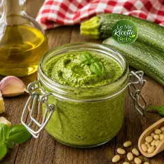 Pesto di zucchine Bimby pronto in un barattolo, con ingredienti freschi come zucchine, basilico, aglio, parmigiano e pinoli.