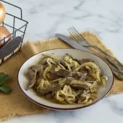 Piatto di fegato alla veneziana con cipolle dorate, accompagnato da due foglie di salvia e cipolle in un cestino.