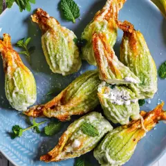 Fiori di zucca fritti, ripieni di formaggio cremoso e guarniti con menta fresca su un piatto blu.