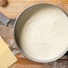 Besciamella cremosa in pentola, con noce moscata e sfoglie per lasagne pronte.
