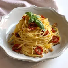 Un piatto di spaghetti conditi con pomodorini gialli secchi, basilico fresco e pangrattato croccante.