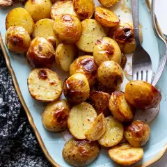 Patate novelle al forno dorate e croccanti, servite su un piatto azzurro con forchette.