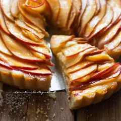 Una fetta di crostata di mele dorata, con mele caramellate disposte a rosa su una base friabile.
