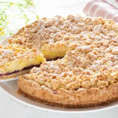 Sbriciolata alla crema con confettura di frutti di bosco, cosparsa di zucchero a velo. Una fetta è stata appena tolta, rivelando il ripieno.