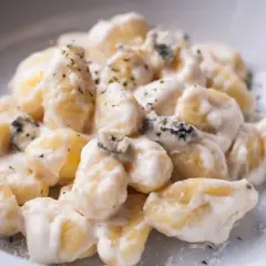 Gnocchi al gorgonzola cremosi, con pezzetti di formaggio blu e erbe aromatiche, serviti in un piatto bianco.