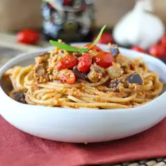 Un piatto invitante di pasta e melanzane alla napoletana, condito con pomodorini freschi e basilico.