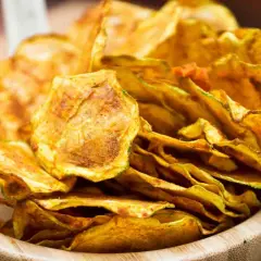Croccanti chips di zucchine dorate, un'alternativa salutare e gustosa alle patatine, servite in una ciotola di legno.