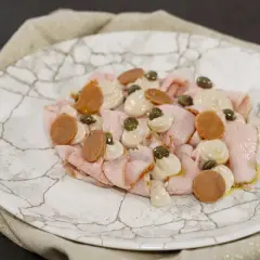 Vitello tonnato ricetta: fettine rosa di vitello, salsa tonnata, capperi e acciughe su piatto di marmo.
