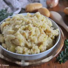 Patate in tecia, un contorno rustico e saporito, servito in una ciotola bianca su un tagliere di legno, con patate crude e erbe aromatiche sullo sfondo.