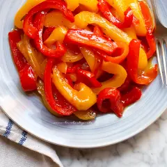 Piatto di peperoni in agrodolce, rossi e gialli, conditi con olio e spezie, pronti per essere gustati.