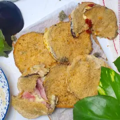 Cordon bleu di melanzane impanati e fritti, ripieni di prosciutto e formaggio filante. Accanto, melanzane fresche e pangrattato.
