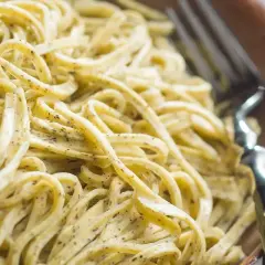 Un primo piatto invitante: tagliolini al limone, conditi con una crema delicata e erbe aromatiche, pronti per essere gustati con una forchetta.