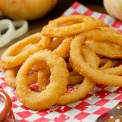 Anelli di cipolla dorati e croccanti, preparati con una **pastella per fritti** perfetta, serviti su carta a quadri rossi con sale grosso.