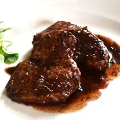 Tre fette di brasato di manzo succulento in salsa scura, guarnite con ribes rossi e menta fresca.