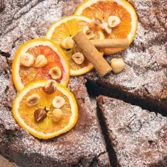 Deliziosa torta di pane al cioccolato, cosparsa di zucchero a velo, decorata con fette d'arancia, nocciole e cannella.