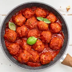 Succulente polpette di carne in padella, immerse in un ricco sugo di pomodoro, guarnite con foglie di basilico fresco.