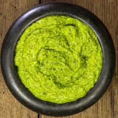 Un mortaio di pietra nera contiene un vibrante pesto alla genovese, pronto per condire la pasta.