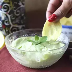 Una mano intinge una patatina in una cremosa maionese con uovo sodo, guarnita con menta.