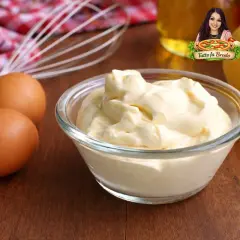 Una ciotola di cremosa maionese fatta in casa, con uova, limone e frusta sullo sfondo.