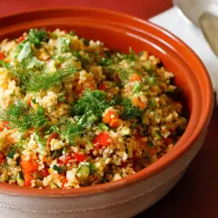 Tabulè di verdure fresco e colorato, con pomodori, zucchine e erbe aromatiche, servito in una ciotola di terracotta.