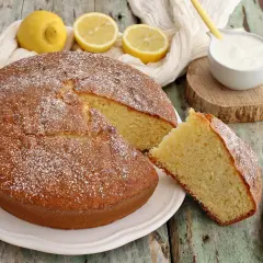 Deliziosa torta per colazione, soffice e profumata al limone, spolverata di zucchero a velo, con una fetta tagliata e una ciotolina di yogurt.
