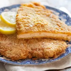 Due cotolette al forno dorate e croccanti, servite su un piatto blu con spicchi di limone.