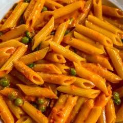 Penne ai 7 peccati, un piatto di pasta avvolto in una cremosa salsa rossa, con piselli verdi che spuntano come gemme preziose.