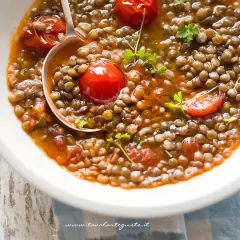Una ciotola di zuppa di lenticchie fumante, con pomodorini e prezzemolo fresco. Un cucchiaio raccoglie una porzione generosa di questo piatto confortante.