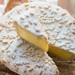 Torta della nonna facile, con crema gialla, pinoli e zucchero a velo. Una fetta è stata tagliata.