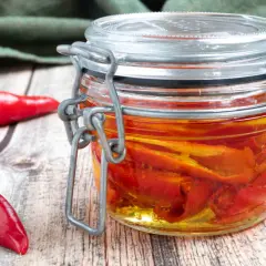 Barattolo di **olio al peperoncino** fatto in casa, con peperoncini rossi freschi accanto su un tavolo di legno.