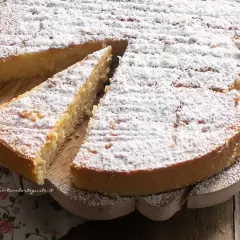 Una fetta di torta di riso, cosparsa di zucchero a velo, attende di essere gustata su un tagliere di legno.